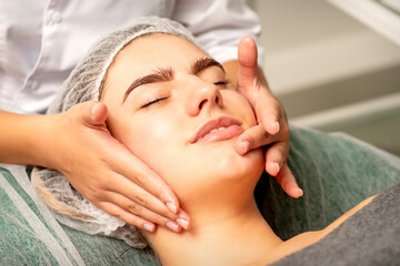 Face massage. Beautiful caucasian young white woman having a facial massage with closed eyes in a...