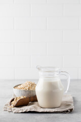 A jug of oat milk, a bowl of oatmeal on the table on a light background. Copy space.