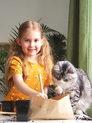 Little toddler girl planting seeds in the pots with cat. Love of pets. Funny and curious pets. Home gardening, transplanting plants, seedlings