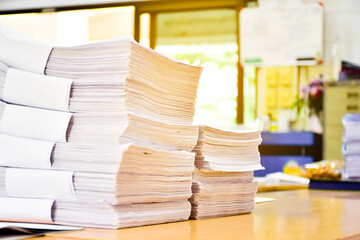 A pile of paper, an important, unfinished work, was piled up on a desk in an office, soft and selective focus.