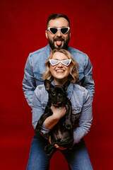 Obraz premium happy couple wearing sunglasses holding a french dog. happy family concept.