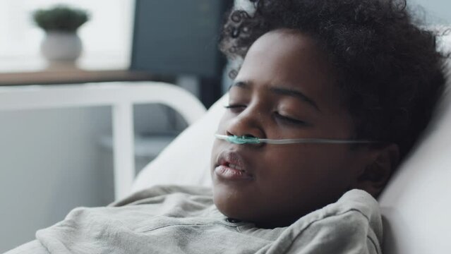 Close-up of African American boy with oxygen tube in nose sleeping in hospital bed at daytime
