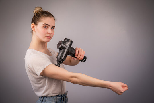 Caucasian woman uses a massager gun for pain in the muscles of the arm.