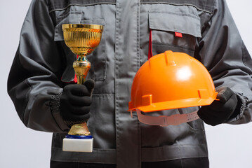Builder contractor with a gpolden award trophy and hardhat in hands close up.