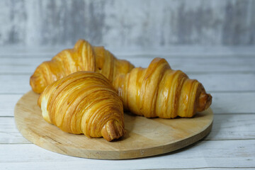 Fresh baked croissants on wooden cutting board on concrete grey surface in dark 