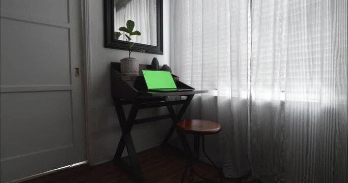 Home office in quiet and focused room with modern desk by dimly lit window. Steadicam slowly pushes in on wide shot. Green-screen for chroma key.