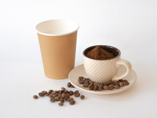 Ground coffee in a cup with a saucer, coffee beans and a disposable paper cup with space for text