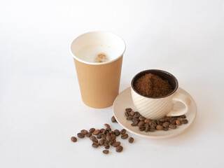 Ground coffee in a cup with a saucer, coffee beans and a disposable paper cup with copy space