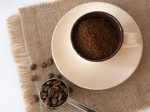 Ground Coffee In A Cup And Saucer On A Canvas Napkin, Coffee Beans Are Scattered And A Serving Spoon. View From Above