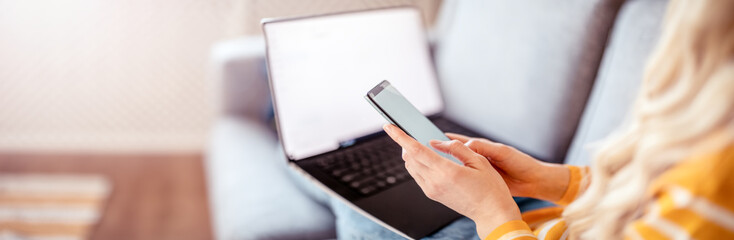 Woman with smartphone in her hands sitting on the couch and working on the laptop
