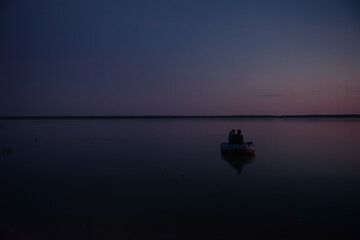Father and son go to night fishing in a boat. Night fishing on the lake. Leisure, joint pastime of his son with his father, a common hobby. The concept of fishing, tourism and rest