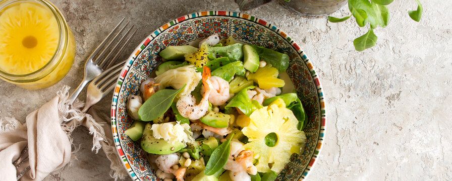 plate with salad with shrimp, spinach, avocado and pineapple on a light table
