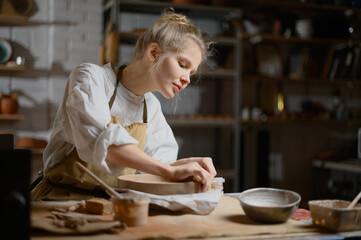 A ceramist makes a plate. Woman in an apron works in a pottery workshop. 