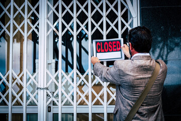 Businesswoman closing her business activity due economy crisis putting closed sign on the door of his store. Concept of bankrupt and shotdown commercial job occupation. Back view of man - obrazy, fototapety, plakaty