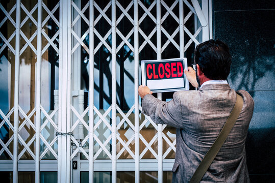 Businesswoman Closing Her Business Activity Due Economy Crisis Putting Closed Sign On The Door Of His Store. Concept Of Bankrupt And Shotdown Commercial Job Occupation. Back View Of Man