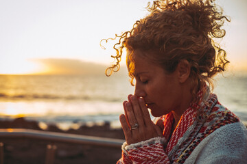Meditation and inner balance interior happiness concept with side portrait of young woman praying and meditating outdoor with sunset ocean in background. Concept of mental health lifestyle
