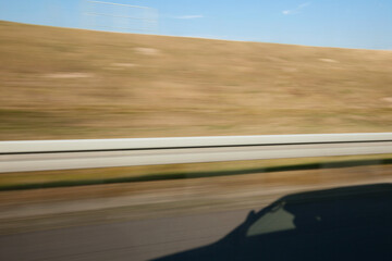 The shadow of a car on an asphalt road, the journey, the motion. Greenery and sky in the background.