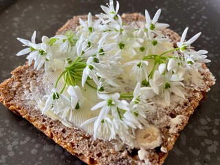 White flowers of wild garlic on slice of homemade sour dough bread, black Nordic ceramic plate.