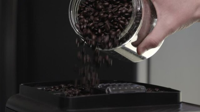 Slow motion close up of coffee beans being poured into coffee maker grinder.