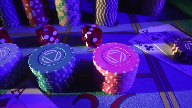 Camera pans over a gaming table with cards, stacks of chips, dice and a dealer chip. Close up of a poker set in a casino in blue light. The concept of gambling, betting in the casino.