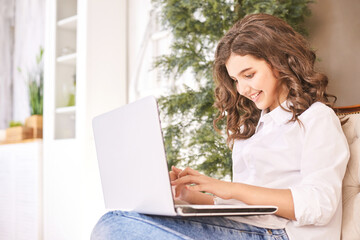 Female teenager laptop on sofa. Glad teen student using netbook for studies. Sitting on couch at home. School online lessons. Browing news. Optimist university girl portrait. Notebook homework