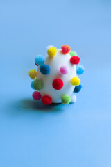 Egg covered with pom-poms on a blue background, funny egg