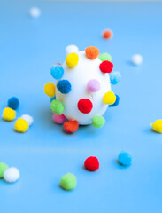 Egg with colorful pom-poms and scattered pom-poms, side view, selective focus