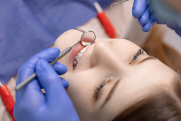 Smiling pretty woman is having her teeth examined by dentist in clinic cleaning, top view