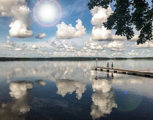 clouds over the lake, odbicie chmur w tafli spokojnego, letniego jeziora, dzieci na pomoście.