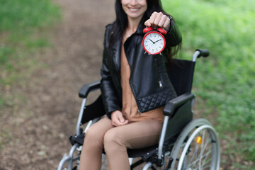 Woman in wheelchair holds red alarm clock in park