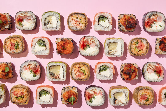 Various sushi rolls on pink background, top view.