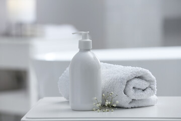 Fototapeta na wymiar Bottle of bubble bath, towel and flowers on white table in bathroom