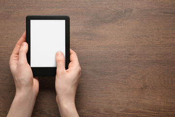 Woman using e-book reader at wooden table, top view. Space for text