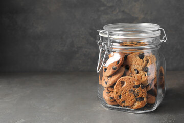 Delicious chocolate chip cookies in glass jar on grey table, space for text