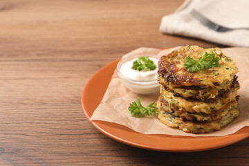 Delicious zucchini pancakes and bowl with sour cream on wooden table. Space for text