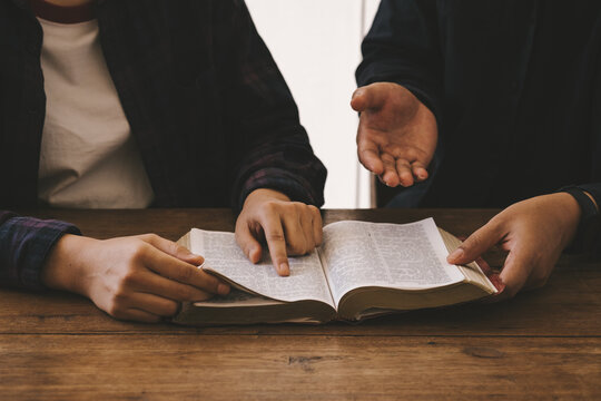 Two christianity sitting around wooden table with open holy bible study reading together in Sunday school. Christian bible god deliver devotional with hand friendship.