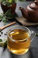 Cup of aromatic sage tea on black table. Space for text