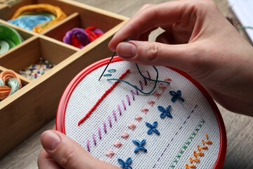 Woman doing different stitches with colorful threads on fabric in embroidery hoop at wooden table, closeup