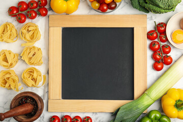 Chalkboard surrounded by different ingredients on white marble table, flat lay with space for text....