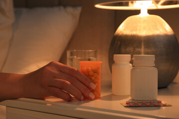 Woman taking pills from nightstand indoors, closeup. Insomnia treatment