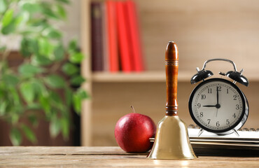 Golden school bell, apple, alarm clock and notebooks on wooden table in classroom, space for text