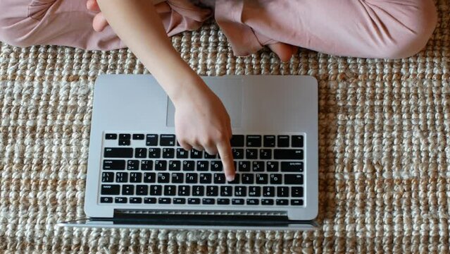 Top view of a child typing on a laptop sitting on a wicker mat