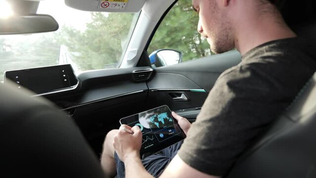 Young male investor checking financial application on tablet while riding car