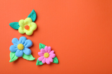 Colorful flowers with leaves made from play dough on orange background, flat lay. Space for text