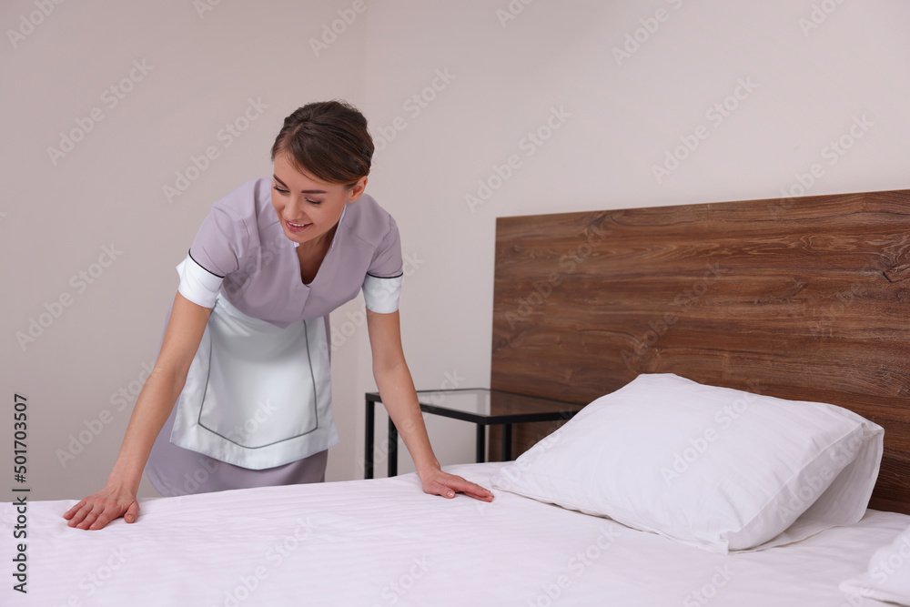 Sticker beautiful chambermaid making bed in hotel room