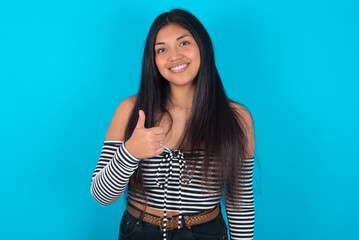 young latin woman wearing striped T-shirt over blue background giving thumb up gesture, good Job!...