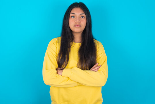 Picture of angry young latin woman wearing yellow sweater over blue background looking camera.