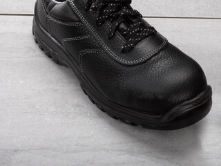 Zapato negro de seguridad sobre fondo de baldosas