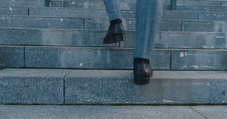 Legs of business man wearing black shoes walking up the stairs outside the business building. Male entrepreneur in formal suit goes to work