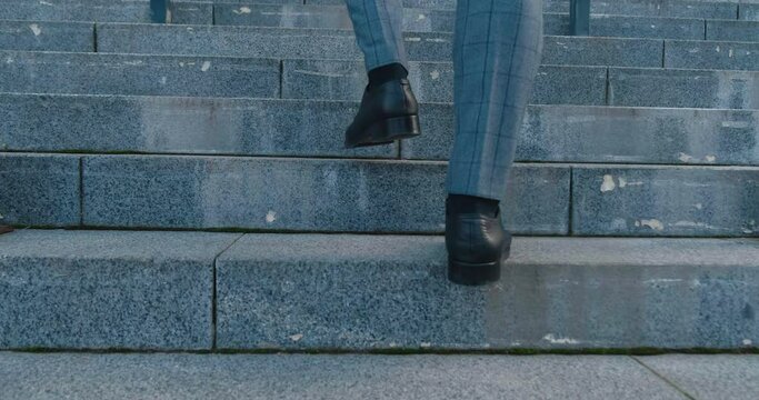 Legs of business man wearing black shoes walking up the stairs outside the business building. Male entrepreneur in formal suit goes to work